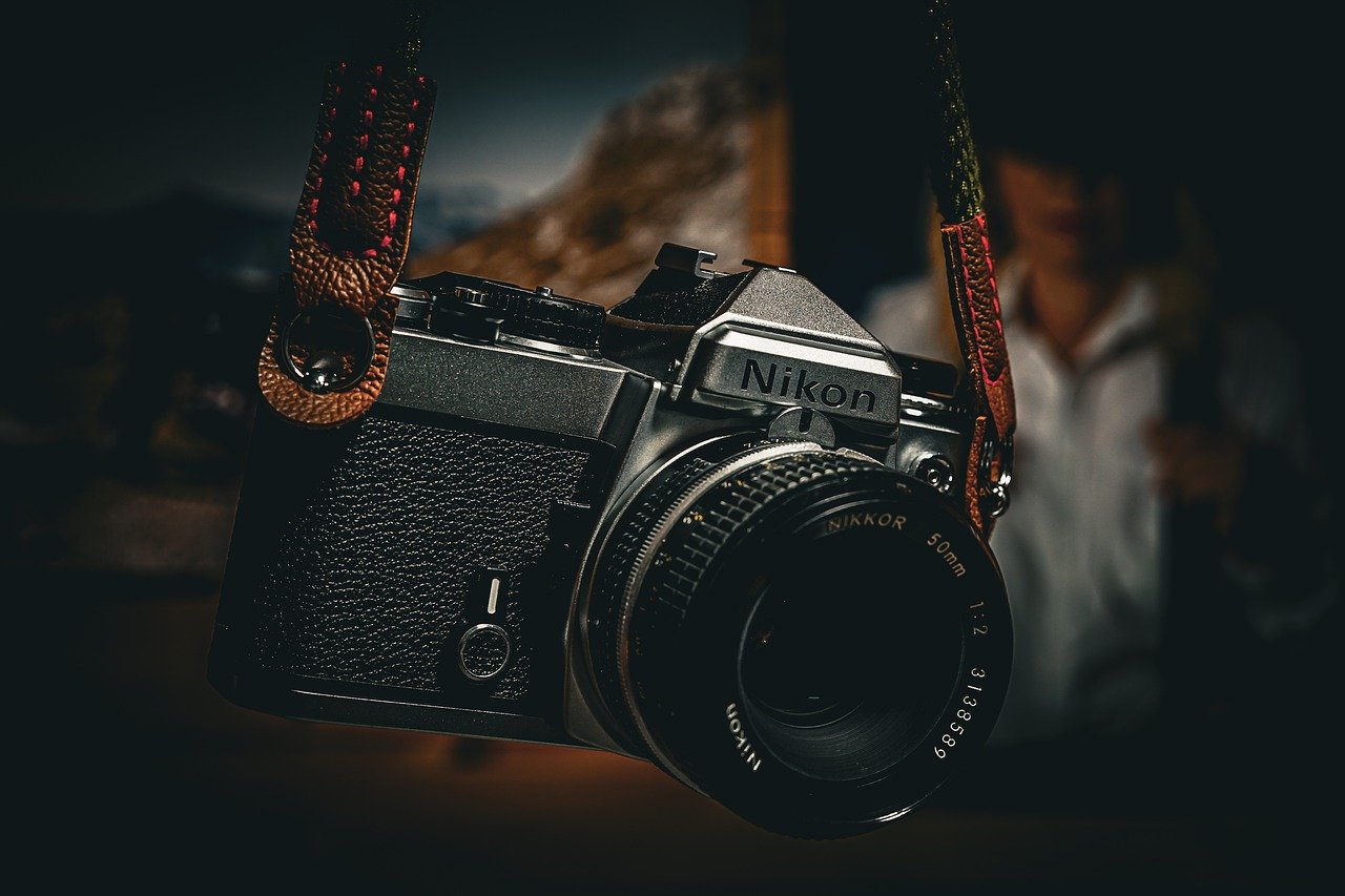 Nikon camera in moody lighting hanging from a leather strap.