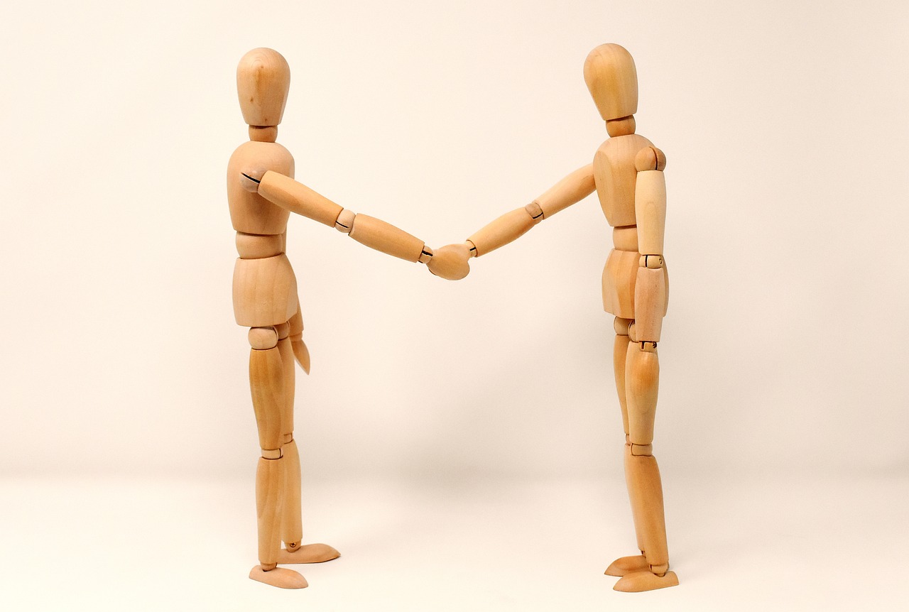 two wooden people shake hands